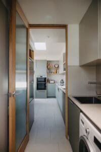Compact Australian laundry and kitchen by Coys Constructions with sage cabinetry, built-in appliances, and modern design flow.
