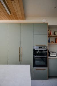 Modern Australian kitchen cabinetry by Coys Constructions with integrated appliances, soft sage finish, and natural timber accents.