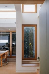 Architectural detail by Coys Constructions featuring timber-framed windows, built-in bench seating, and natural garden views.