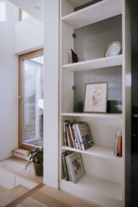 Built-in bookshelf by Coys Constructions with curated books, decorative art, and ribbed glass backing beside a timber-framed window.