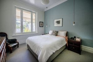 Elegant bedroom by Coys Constructions with soft blue feature wall, pendant lighting, and heritage-style window detailing.