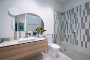 HAWTHORN Contemporary bathroom by Coys Constructions featuring vertical mosaic tiles, floating vanity, round mirror, and walk-in shower.