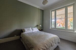 HAWTHORN Peaceful bedroom by Coys Constructions with soft green feature wall, large window, and garden view showcasing autumn foliage.