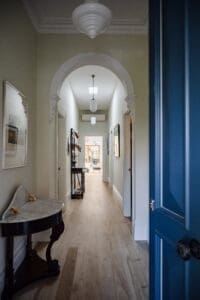 Heritage-style hallway by Coys Constructions with timber flooring, ornate archway, and a view into a sunlit living space.