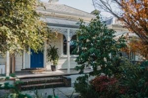 MARIAN HAWTHORN Restored heritage home in Victoria with blue door, ornate fretwork, and lush native garden – built by Coys Constructions.